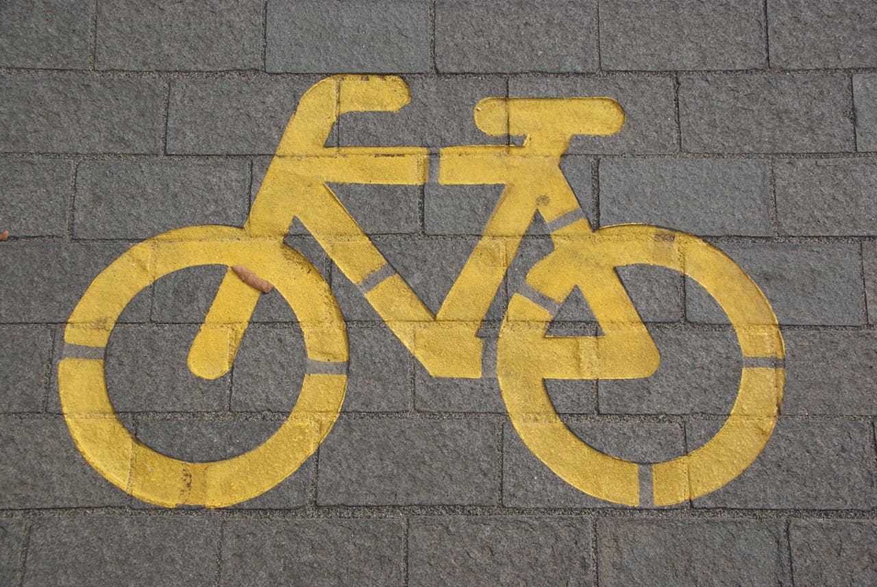 Bright yellow bicycle symbol on gray pavement marking a bike lane.